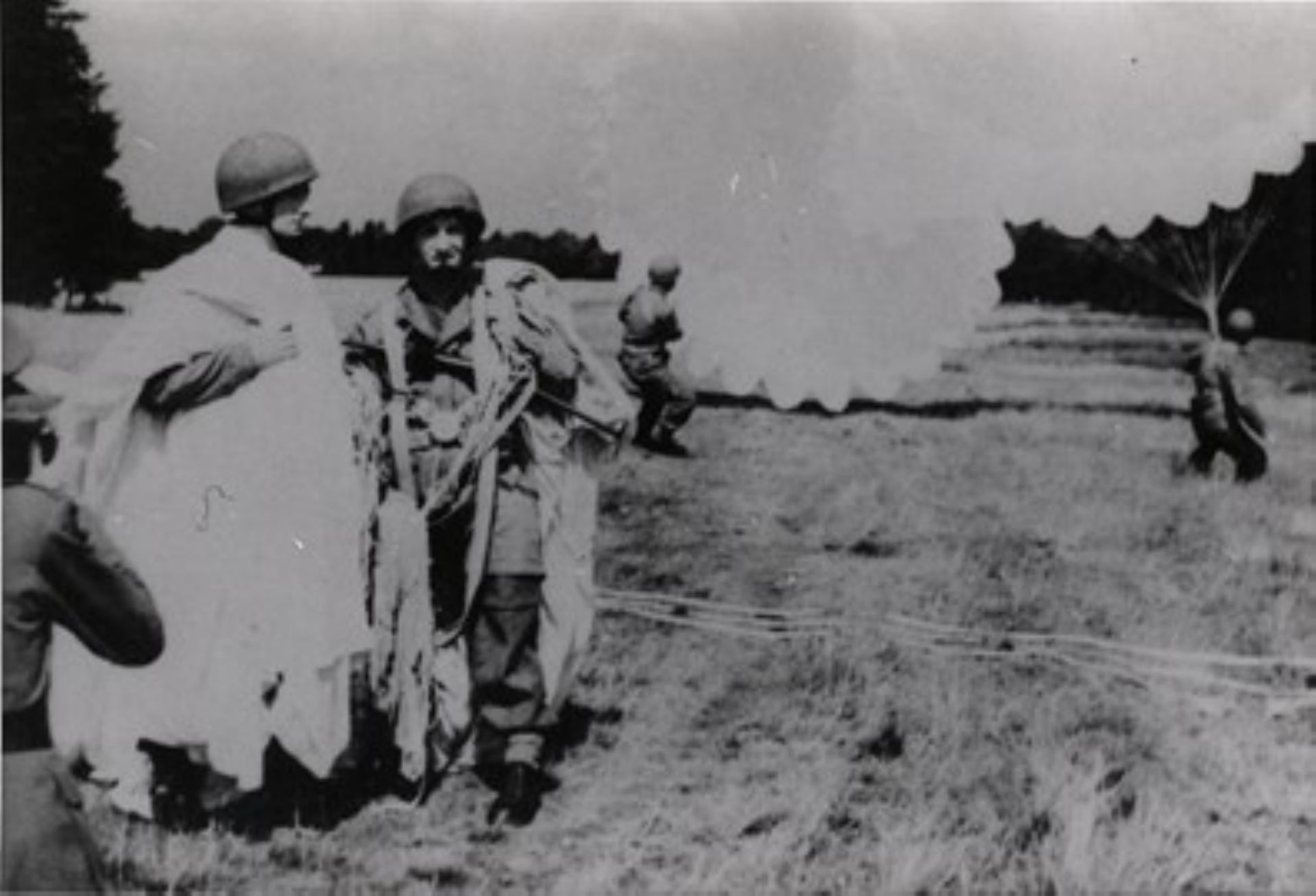 De parachutisten zijn geland en lopen met hun parachute onder hun arm weg.