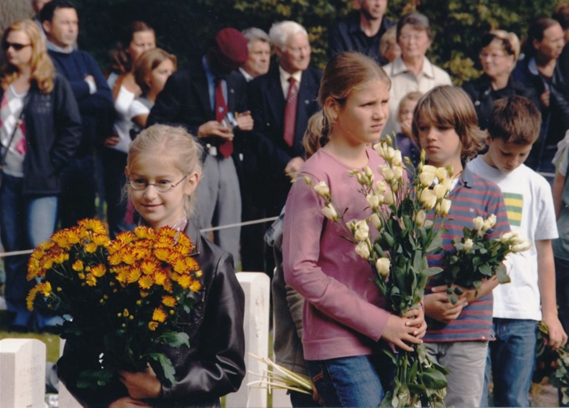 Kleurenfoto waarop bloemkinderen staan die bloemen leggen bij de graven.